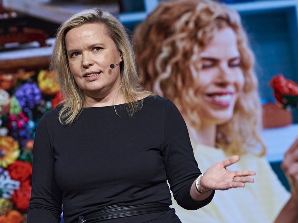 Adriana Jahňáková speaking on stage with a headset microphone at a corporate event.