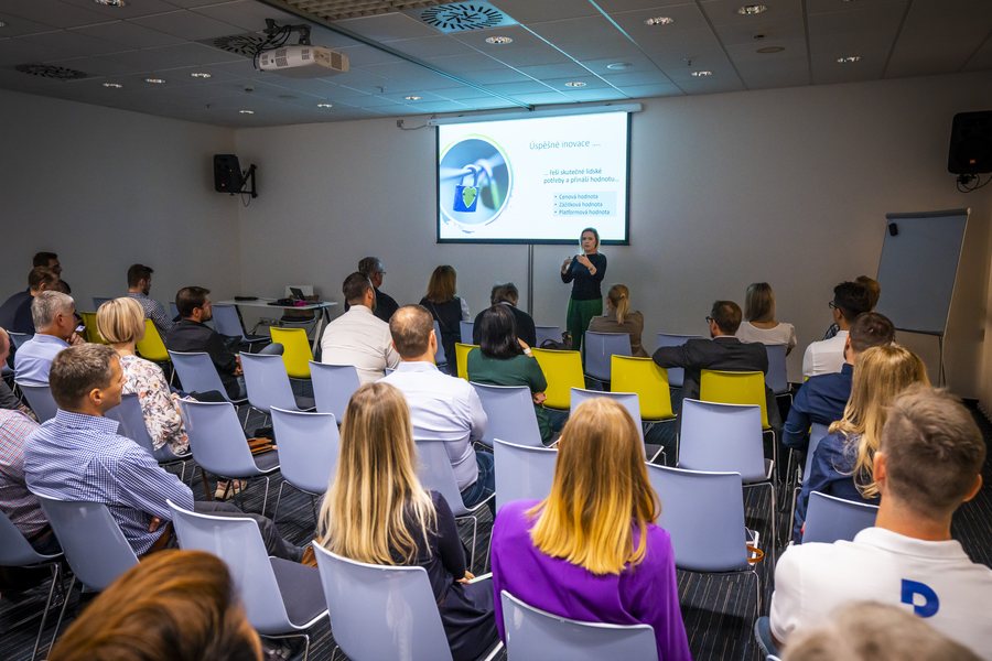 Adriana Jahňáková presenting to a seated audience in a workshop room.